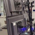 A multi-monitor computer workstation setup with adjustable mounting arms in what appears to be a laboratory or technical workspace environment