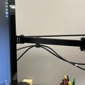 A computer monitor on an adjustable arm mount with cables, positioned above a desk organizer containing pens and office supplies