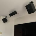 Three black speakers mounted on white ceiling above a large dark TV screen
