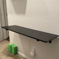 Wall-mounted black desk or shelf with green storage boxes underneath, next to a white door in a room with textured walls