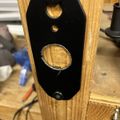 Black metal plate with circular openings mounted on wooden frame in workshop setting