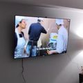Wall-mounted TV displaying a cooking show with chefs in white uniforms working in a kitchen, with PBS logo visible in corner