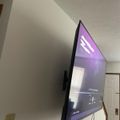 Large flat-screen TV mounted on white wall displaying purple-tinted content in a residential room with textured ceiling