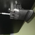 A gray mechanical clamp or mounting bracket attached to a black surface with a threaded adjustment screw