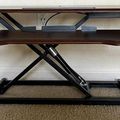 Height-adjustable standing desk converter with wooden surface and black metal frame on carpeted floor