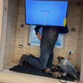 Person installing a wall-mounted TV in a wooden interior space with tools on the floor