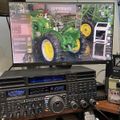 Ham radio equipment setup with multiple transceivers and a computer monitor displaying a green John Deere tractor