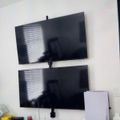 Two flat-screen TVs mounted vertically on a white wall above a desk with various items and equipment.