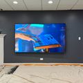A large wall-mounted TV displaying someone playing a keyboard, positioned above a fireplace in a room under construction with exposed flooring and construction materials visible