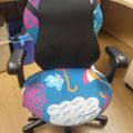 Office chair with colorful weather-themed fabric cover featuring clouds, raindrops, and umbrellas in blue, pink, and white colors, positioned at a wooden desk in an office setting