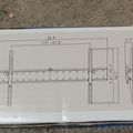 Technical drawing or blueprint showing dimensions and measurements for what appears to be a mounting bracket or hardware component, drawn on white paper placed on a concrete surface