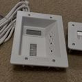 Two white wall-mounted control panels with displays and cables on a textured surface