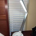 White LED desk lamp with adjustable arm and circular base on wooden surface near window blinds