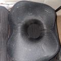 A black mesh office chair seat with visible wear and an indented circular pattern in the center, sitting on a striped rug in an office setting.