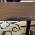 A wooden desk or table with rounded corners and black legs, featuring a green rectangular panel in the center, positioned on a patterned area rug