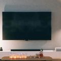 Modern living room with wall-mounted TV above white media console, decorative candles, potted plant, and floor lamp