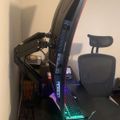 A computer workstation setup with a curved monitor on an adjustable arm, illuminated keyboard with green backlighting, and an ergonomic office chair with headrest
