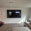 Modern living room with wall-mounted TV, gray sectional sofa, hardwood floors, and natural light from windows