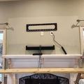 Living room with white fireplace mantel, exposed ceiling beams, and wall-mounted TV installation in progress with visible cables and mounting brackets