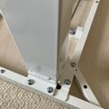 White metal adjustable table or desk leg mechanism with hinges and screws on wooden floor