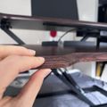 Hand holding a thin wooden object near a 3D printer with printed materials visible on the build plate
