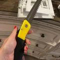Hand holding a folding saw with yellow and black handle, with white cabinet doors visible in the background