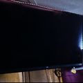 Large flat screen TV mounted on wall with LED strip lighting around the edges in a dimly lit room