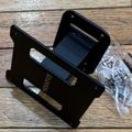 Black plastic device stand or mount with hardware screws in plastic bag on wooden surface