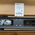 Unboxed TV wall mount kit showing metal mounting bracket, hardware bag, and installation manual in cardboard packaging