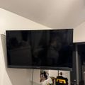 A wall-mounted Sony TV above a white dresser with various tools and equipment including what appears to be DeWalt power tools and a tool bag