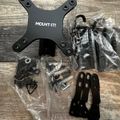Computer monitor mounting hardware kit with black metal brackets, screws, and assembly components laid out on wooden surface