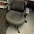 Black office chair with mesh back and fabric seat on clear chair mat in office setting