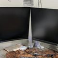 Two black computer monitors on a desk with various cables and items scattered around them