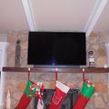 Living room with stone fireplace, mounted TV, white built-in shelving, and Christmas stockings hanging from wooden mantel