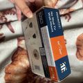 A person holding a blue and orange product box on a patterned blanket with burgundy and white colors. The box appears to be a home improvement or hardware item with text visible on its packaging.