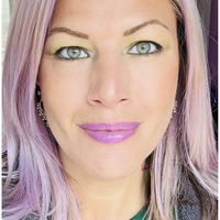 A woman with purple-tinted hair and colorful makeup taking a selfie using a mobile camera app with various filter options visible at the bottom of the screen