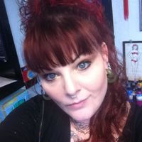 A person with red curly hair and bangs taking a selfie indoors