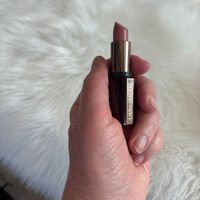 Hand holding a Laura Mercier lipstick with rose-colored tip against white fur background