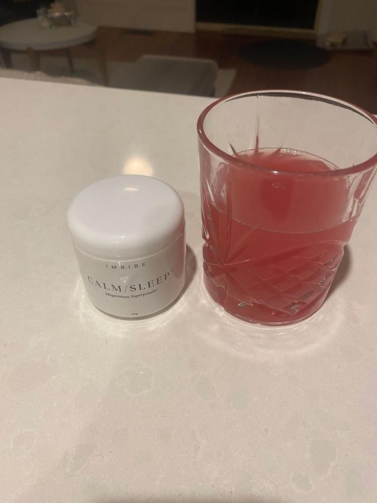 A CALM/SLEEP jar beside a glass of red drink on white marble