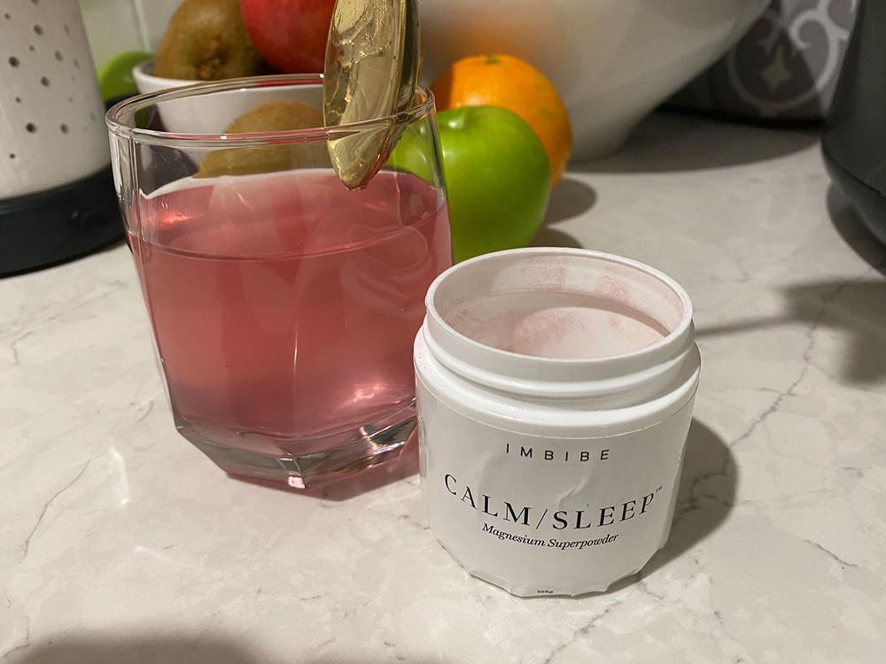 A glass of pink drink beside an open CALM/SLEEP jar on a marble counter