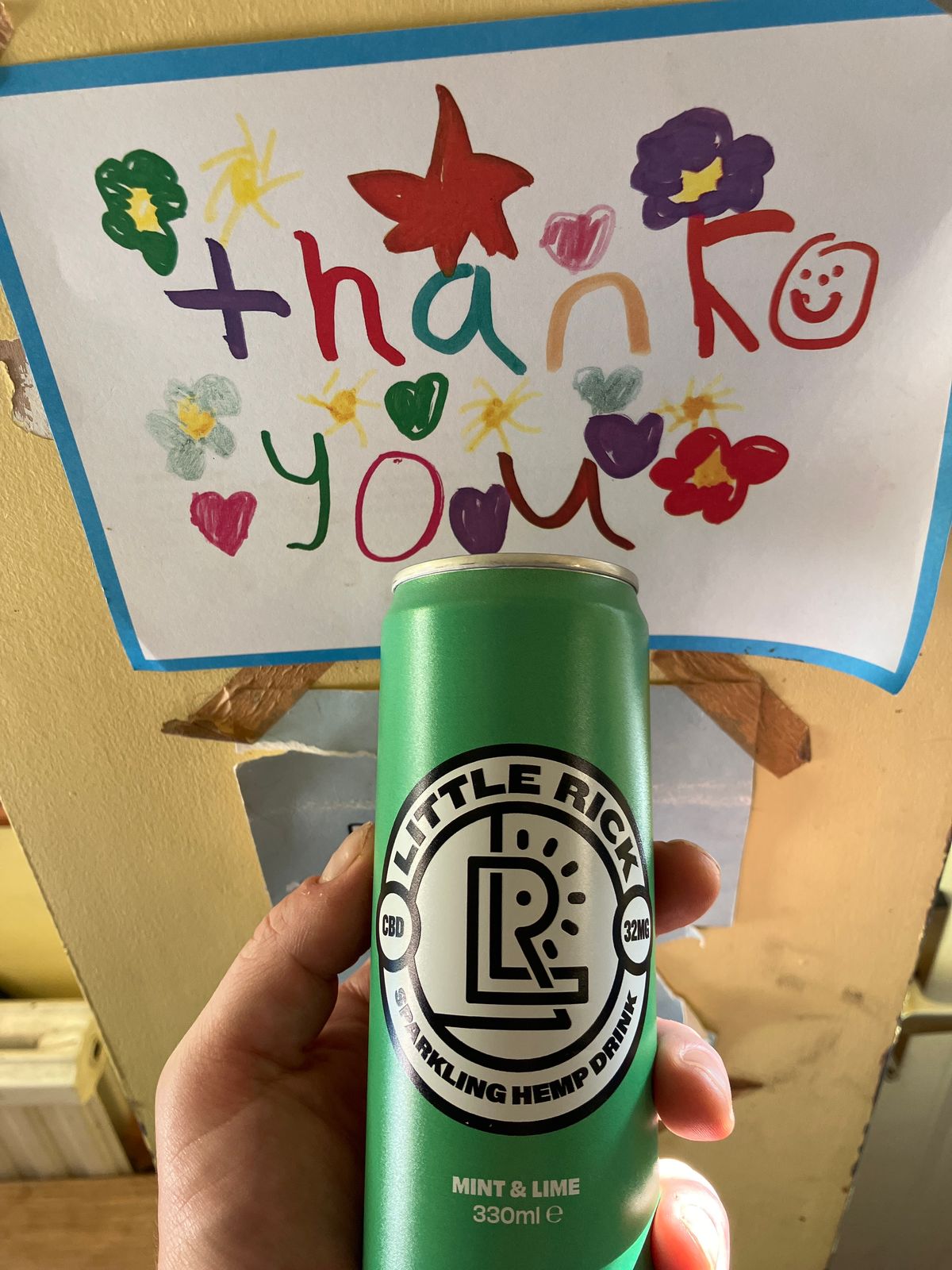 A hand holding a green can of Little Rick sparkling hemp drink in mint and lime flavor, positioned in front of a handmade thank you card decorated with colorful flowers, hearts, and smiley faces.