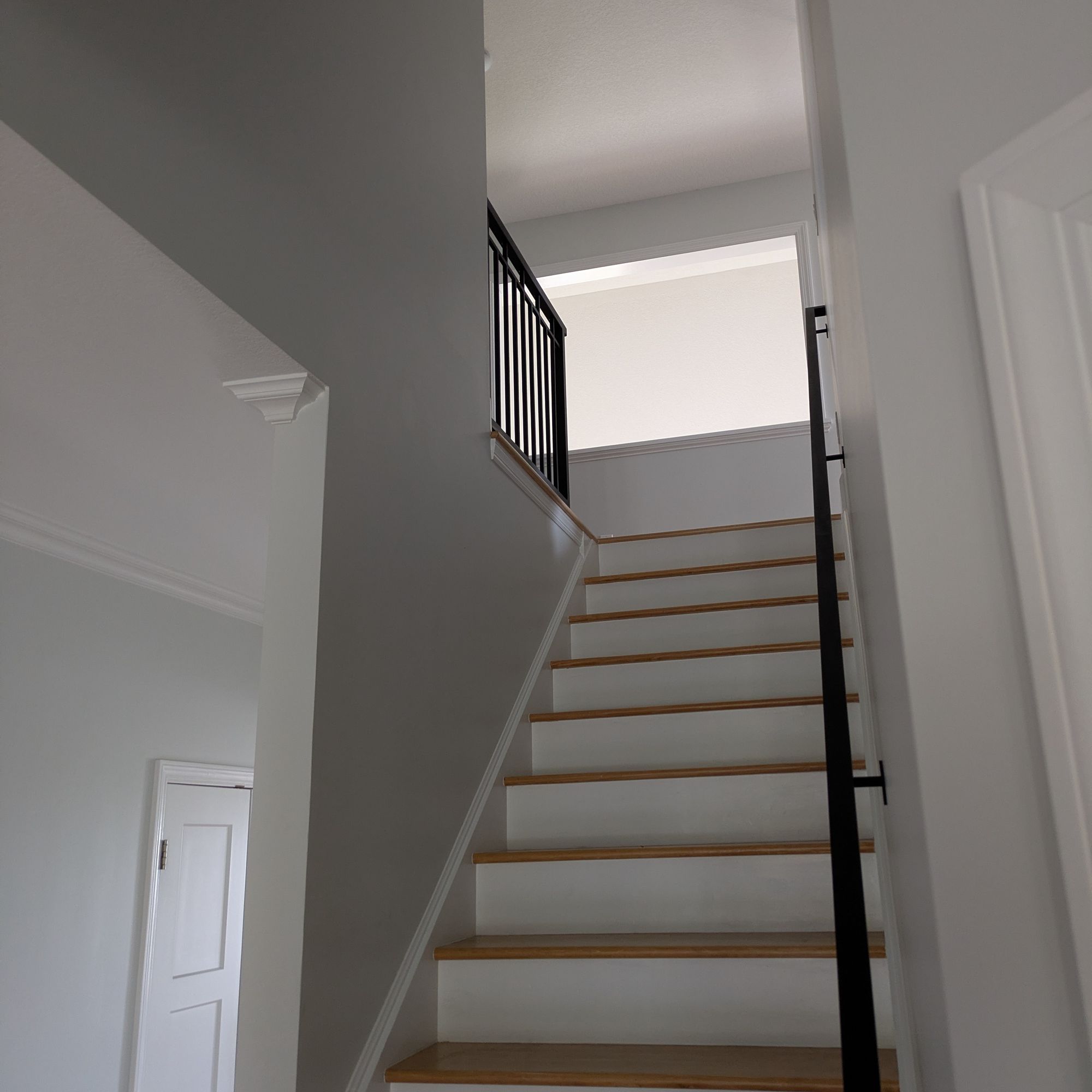 Interior staircase with white risers, wood treads, and black metal railing leading to upper floor