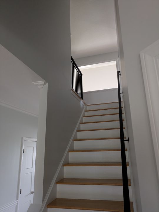 Interior staircase with white risers, wood treads, and black metal railing leading to upper floor