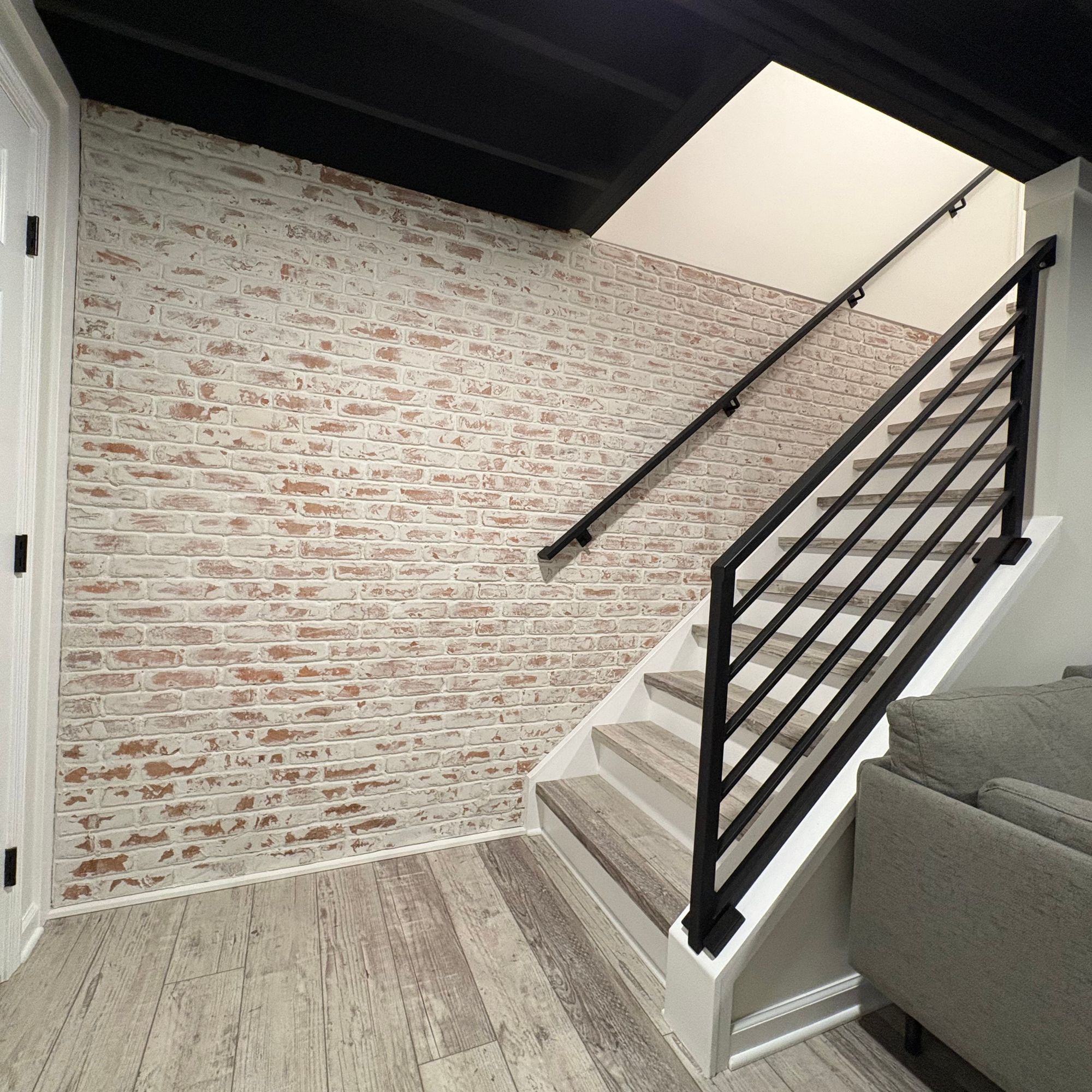 Interior staircase with white painted steps, black metal railing, exposed brick wall, and dark wood beam ceiling