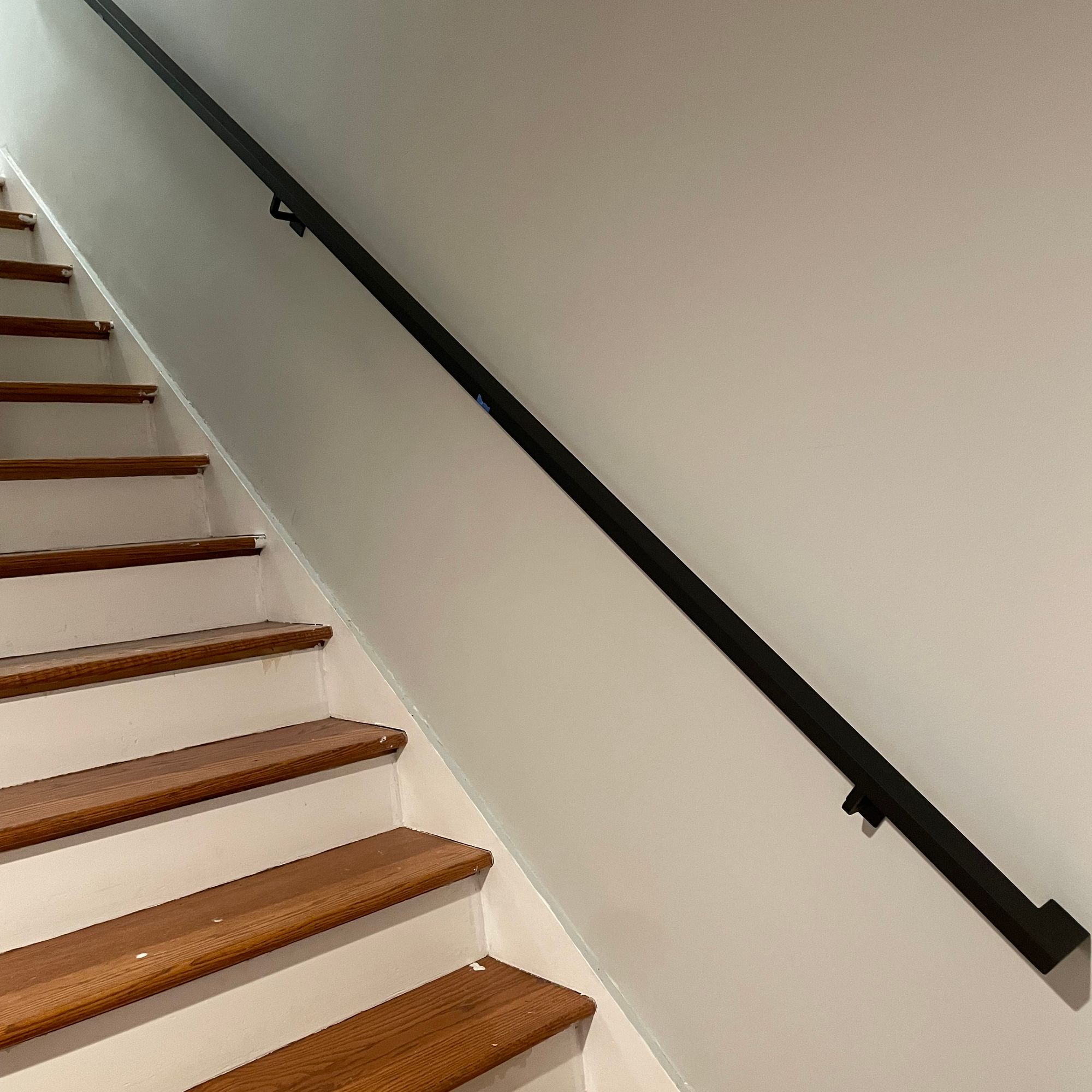 Interior staircase with wooden steps and white risers, featuring a black handrail mounted on white walls