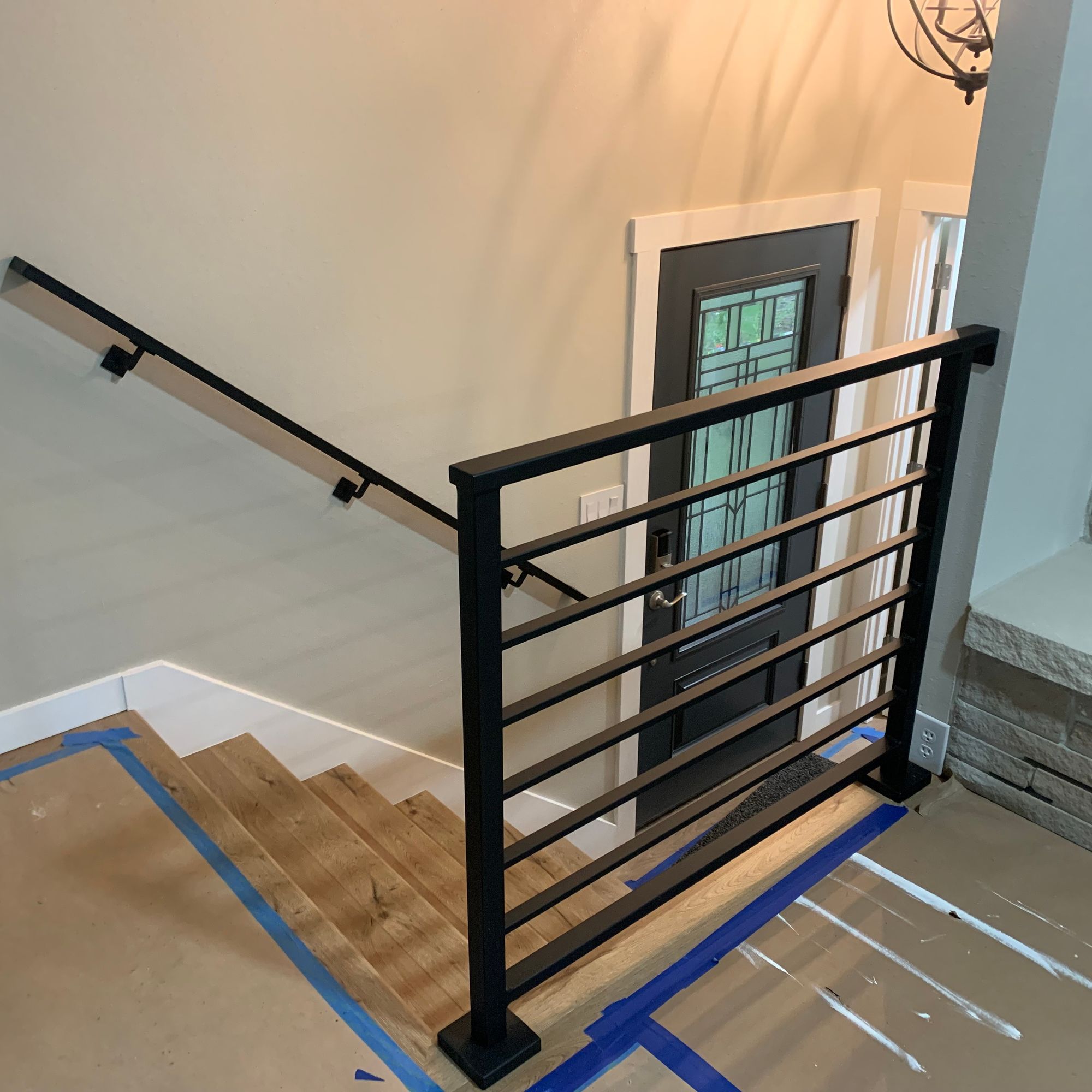 Modern black metal stair railing with horizontal bars in a home interior under construction, with protective blue tape on wooden floors