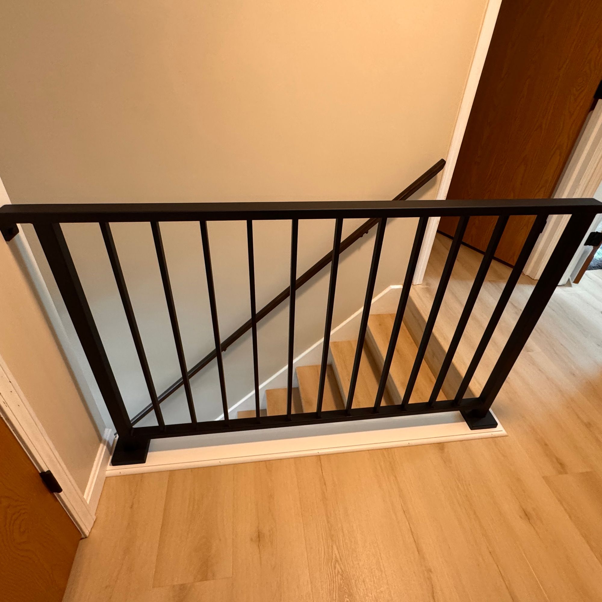 Black metal safety gate installed at the top of wooden stairs with vertical spindle railings