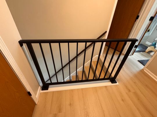 Black metal safety gate installed at the top of wooden stairs with vertical spindle railings