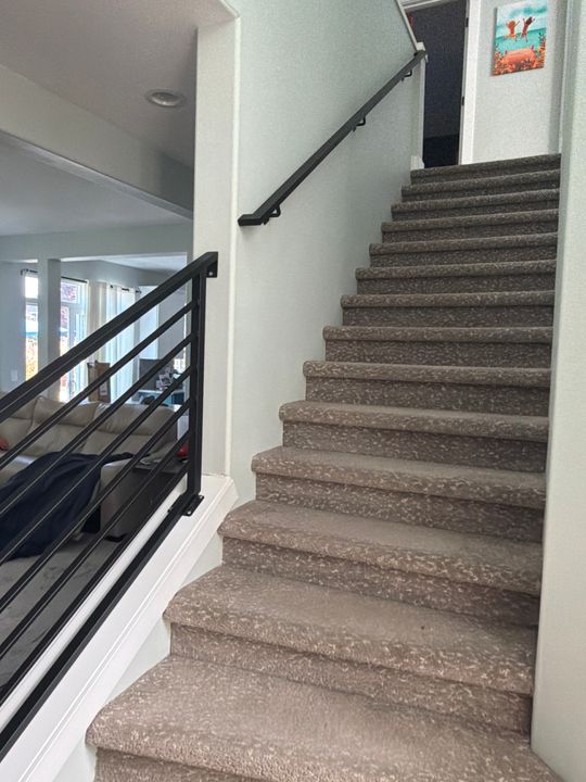 Interior staircase with beige carpeted steps, black metal railings, and white walls in a modern home
