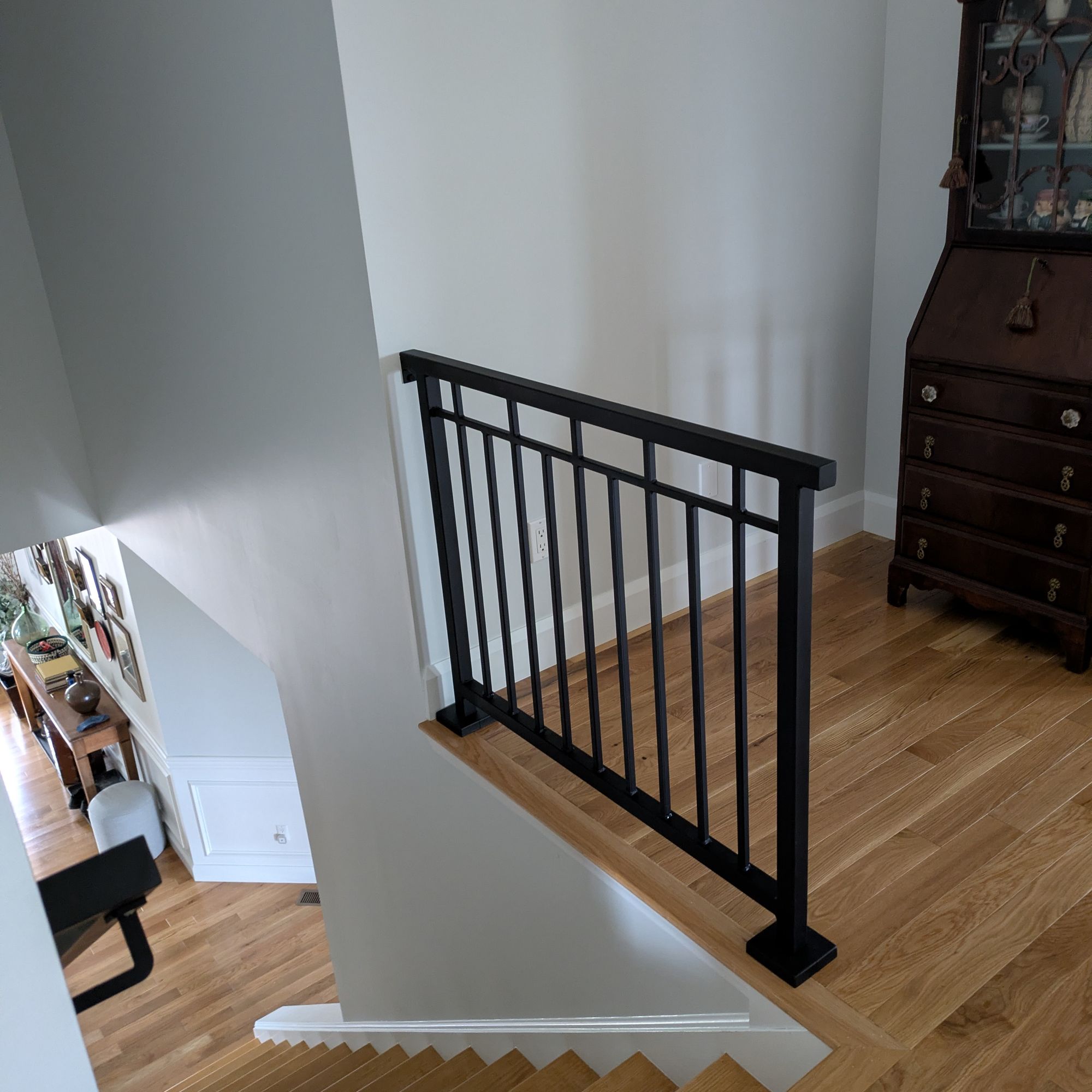 Interior staircase with black metal railing, wooden floors, and antique cabinet on upper landing